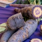 En la imagen se ven unas zanahorias moradas sobre una mesa con un mantel morado